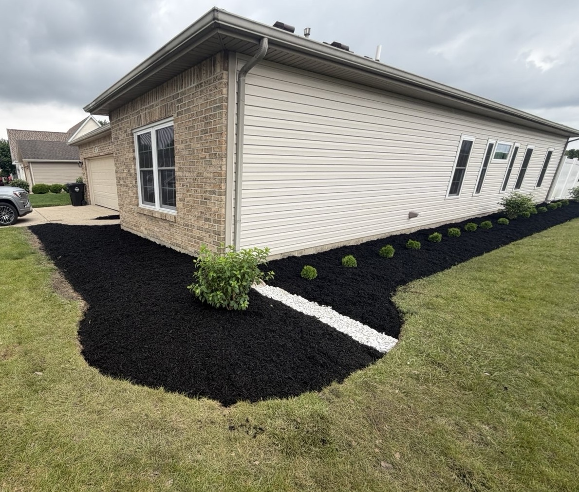 Fresh black mulch, neatly planted shrubs and a white stone accent around a home